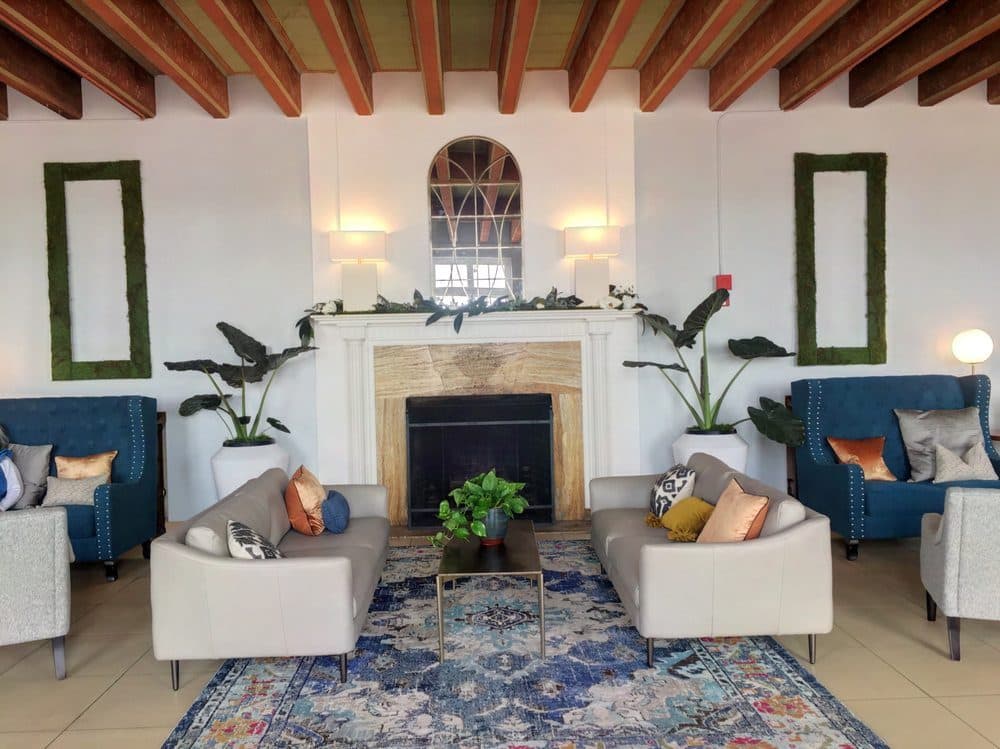 The lobby at Portola Gardens, a warm common room with a stone fireplace, beamed ceiling and comfortable seating
